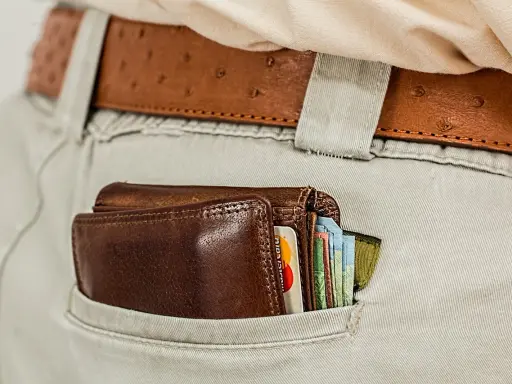 Brązowy portfel z kartami i banknotami w tylnej kieszeni spodni. To symbol oszczędności i strategii franszyza redukcyjna.