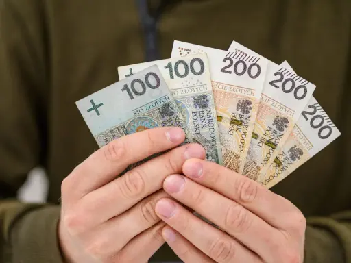 Dłonie trzymają polskie banknoty: 100 i 200 zł. Może to być zwrot OC dla niepełnosprawnych lub po prostu wypłata.