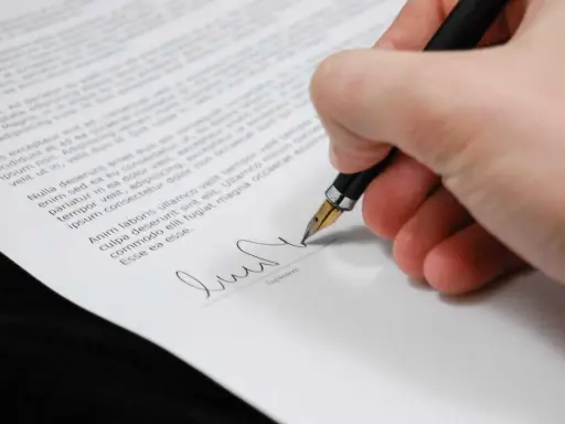 Podpisanie dokumentu, który może być upoważnieniem do rejestracji pojazdu. Długopis z piórkiem na białym papierze.