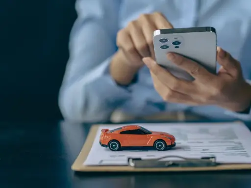 Pomarańczowy mini **casco** na dokumentach, obok dłoni trzymającej smartfon.