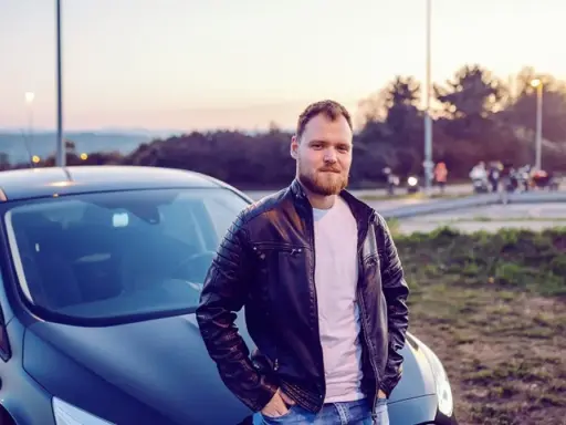 Mężczyzna w skórzanej kurtce opiera się o swój nowy samochód. To jego oc mubi, gotowy na przygodę.