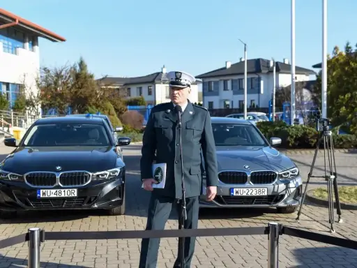 Funkcjonariusz w mundurze stoi między dwoma nieoznakowanymi radiowozami BMW.