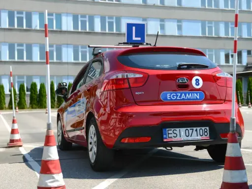 Czerwony samochód z literą "L" na dachu i napisem "EGZAMIN" na klapie. Na placu manewrowym, gdzie można sprawdzić, ile błędów można zrobić na egzaminie teoretycznym na prawo jazdy.