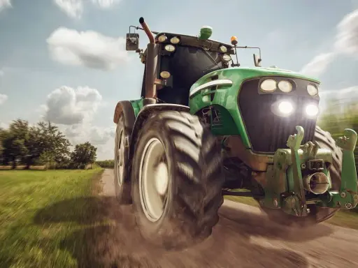 Zielony traktor pędzi po polnej drodze, gotowy do pracy. To maszyna rolnicza, której zakup jest ważną umową kupna sprzedaży.