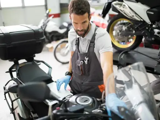 Mechanik w warsztacie sprawdza przegląd motocykla po terminie, używając laptopa do diagnostyki.