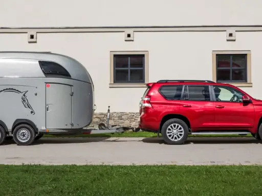 Czerwony SUV holuje przyczepę kempingową z wizerunkiem konia. Jaka kategoria na auto? To idealny zestaw do transportu zwierząt.