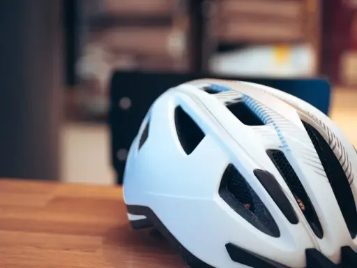Biały kask rowerowy na drewnianym stole. Pamiętaj o bezpieczeństwie, bo jazda bez kasku to mandat.
