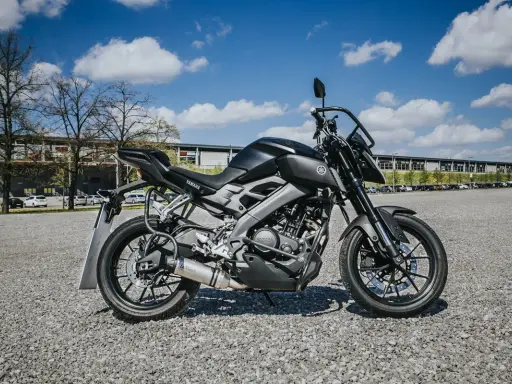 Czarny motocykl Yamaha, idealny na pierwsze prawo jazdy a1, stoi na żwirowym placu przed budynkiem.