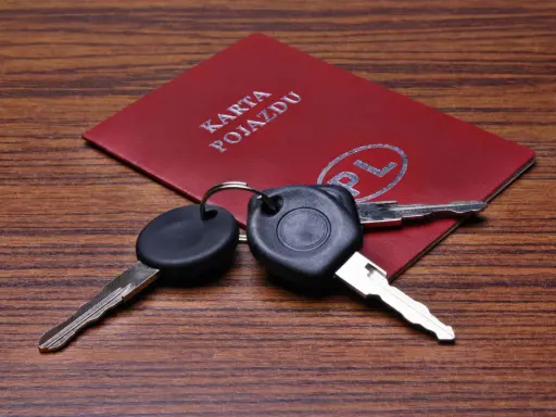 Kluczyki samochodowe leżą na czerwonej karcie pojazdu z napisem "KARTA POJAZDU" i symbolem "PL".