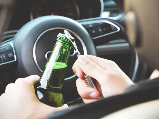 Ręce otwierające butelkę piwa za kierownicą. Pamiętaj, że od 0,2 promila zabierają auto.