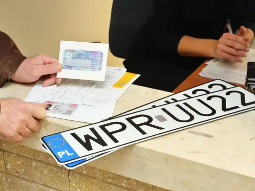 Nowe rejestracje samochodowe leżą na ladzie urzędu. Klient pokazuje dokumenty do rejestracji pojazdu.