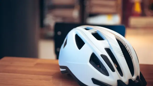 Biały kask rowerowy na drewnianym stole. Pamiętaj o bezpieczeństwie, bo jazda bez kasku to mandat.