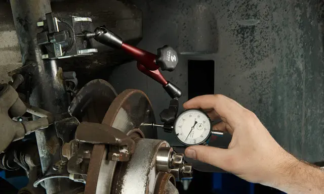 Mechanik mierzy bicie tarczy hamulcowej, by zdiagnozować drgania kierownicy przy hamowaniu.