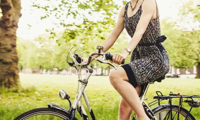Kobieta w letniej sukience cieszy się przejażdżką rowerową po parku.