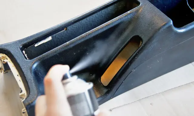 Ręka trzyma puszkę z farbą w sprayu, malowanie elementu konsoli środkowej samochodu.