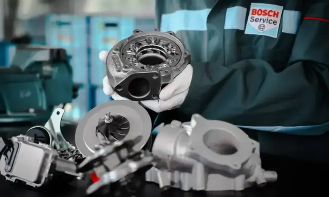 Mechanik w rękawiczkach prezentuje części do regeneracji turbo. W tle logo Bosch Service.
