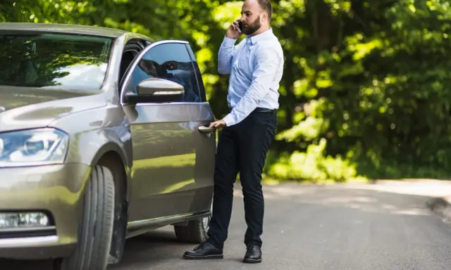 Mężczyzna rozmawia przez telefon, stojąc przy otwartych drzwiach swojego samochodu. Wygląda, jakby potrzebował pomocy, a nie jakby zostawił porzucone samochody.