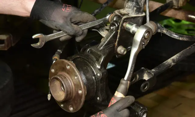 Mechanik dokręca śruby przy piaście, wymieniając łożysko w samochodzie.
