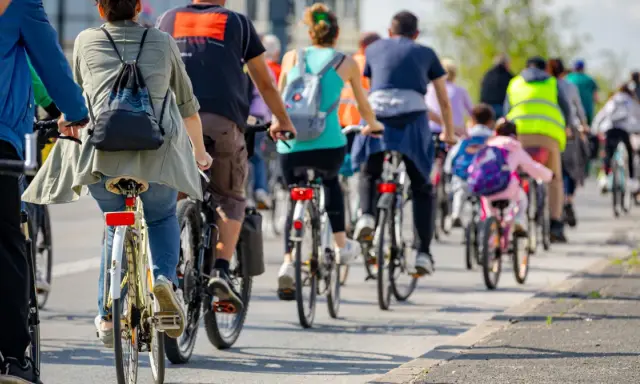 Grupa rowerzystów jedzie w kolumnie, przestrzegając przepisów. Widać plecaki i kamizelki odblaskowe.