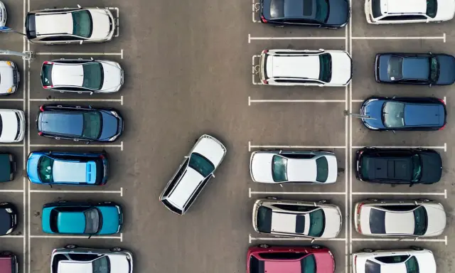Widok z góry na parking z wieloma samochodami. Jeden biały samochód jest zaparkowany tyłem, pokazując, jak parkować tyłem.