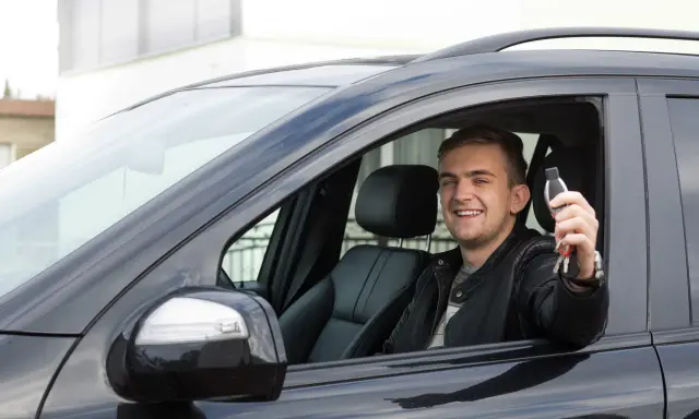 Szczęśliwy młody mężczyzna w czarnej skórzanej kurtce trzyma kluczyki do nowego auta, świeżo po rejestracji pojazdu z Niemiec.