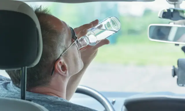 Mężczyzna pije alkohol za kierownicą. Pamiętaj, jaka kara za jazdę pod wpływem alkoholu jest surowa.