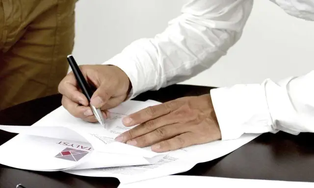Mężczyzna podpisuje dokumenty, stając się ubezpieczającym dla ubezpieczonego. Na papierze widoczne logo firmy.