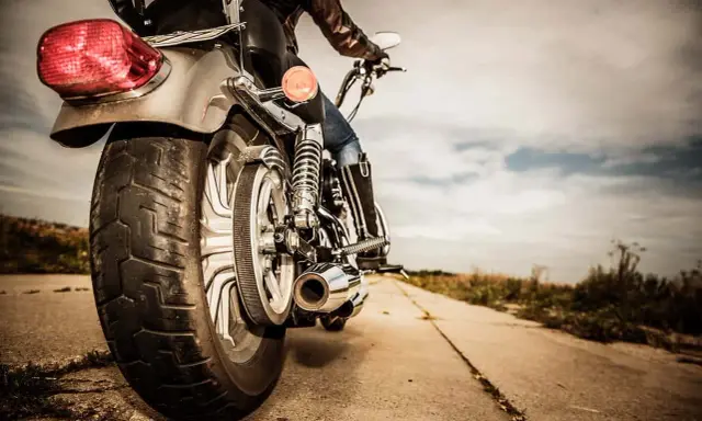 Osoba na motocyklu, widok z tyłu. Błyszczące chromy, skórzana kurtka i dżinsy. Droga prowadzi w dal, pod chmurami.