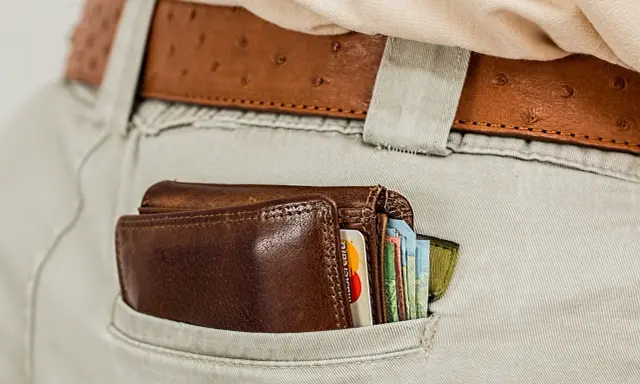Brązowy portfel z kartami i banknotami w tylnej kieszeni spodni. To symbol oszczędności i strategii franszyza redukcyjna.