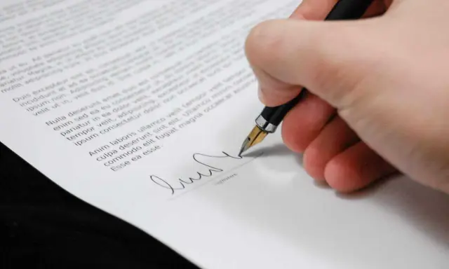 Podpisanie dokumentu, który może być upoważnieniem do rejestracji pojazdu. Długopis z piórkiem na białym papierze.