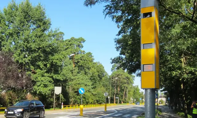 Żółty fotoradar stoi przy drodze, gotowy do rejestrowania prędkości. Z jakiej odległości łapie fotoradar? Z tej, która zapewni bezpieczeństwo.