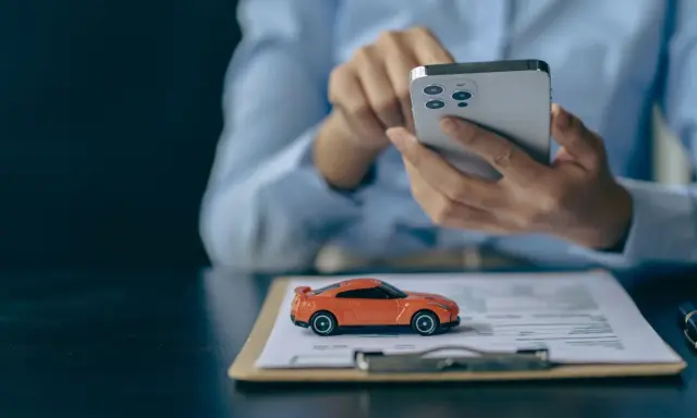 Pomarańczowy mini **casco** na dokumentach, obok dłoni trzymającej smartfon.