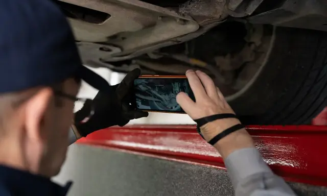 Mechanik używa telefonu do dokumentowania podwozia auta, szukając numerów VIN.