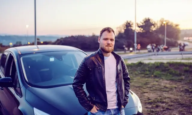 Mężczyzna w skórzanej kurtce opiera się o swój nowy samochód. To jego oc mubi, gotowy na przygodę.
