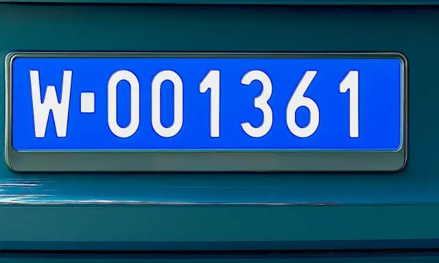 Niebieskie tablice rejestracyjne z numerem W-001361 na ciemnozielonym samochodzie.