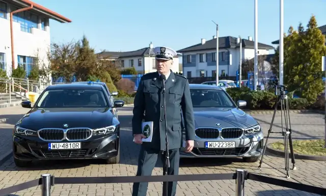 Funkcjonariusz w mundurze stoi między dwoma nieoznakowanymi radiowozami BMW.