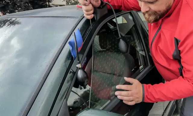 Mężczyzna używa pompki i narzędzia do otwierania drzwi, gdy zatrzasnął kluczyki w samochodzie. Jak otworzyć auto bez kluczyka?