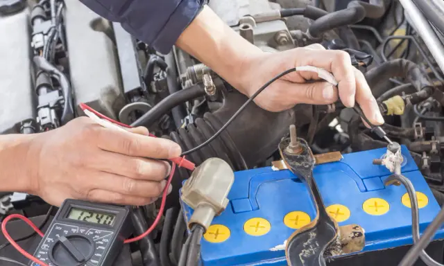 Mechanik sprawdza napięcie akumulatora za pomocą multimetru. Wynik 12.48V wskazuje na jego stan.