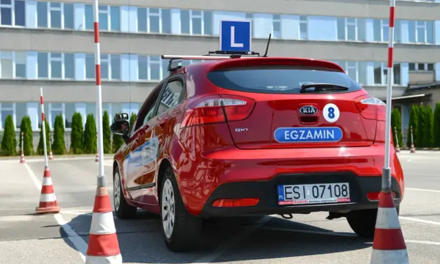 Czerwony samochód z literą "L" na dachu i napisem "EGZAMIN" na klapie. Na placu manewrowym, gdzie można sprawdzić, ile błędów można zrobić na egzaminie teoretycznym na prawo jazdy.