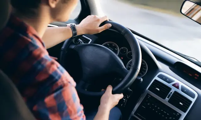 Mężczyzna w kratę prowadzi auto, kluczyki wiszą przy kierownicy. Czy AC przechodzi na nowego właściciela?