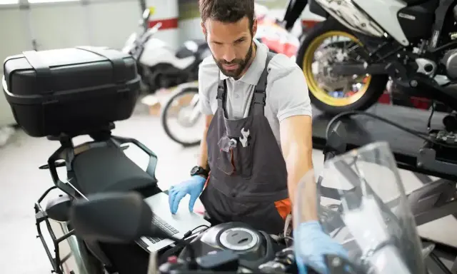 Mechanik w warsztacie sprawdza przegląd motocykla po terminie, używając laptopa do diagnostyki.