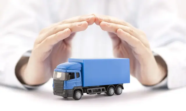 Ręce chronią niebieską ciężarówkę, symbolizując ubezpieczenie AC w kosztach transportu.