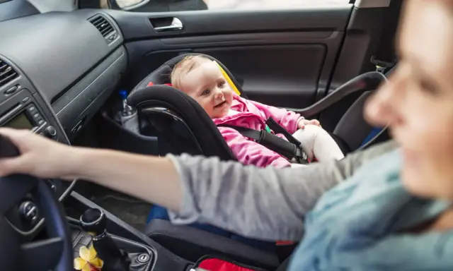 Uśmiechnięte dziecko w foteliku z przodu. Od kiedy dziecko może jeździć z przodu, zależy od jego wieku i wagi.