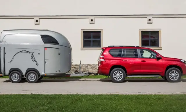 Czerwony SUV holuje przyczepę kempingową z wizerunkiem konia. Jaka kategoria na auto? To idealny zestaw do transportu zwierząt.