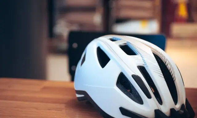 Biały kask rowerowy na drewnianym stole. Pamiętaj o bezpieczeństwie, bo jazda bez kasku to mandat.