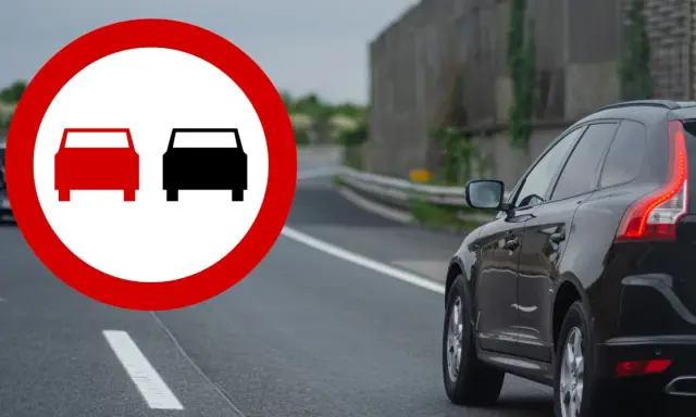 Znak zakazu wyprzedzania na podwójnej ciągłej. Czarny SUV jedzie po drodze, a na pierwszym planie znak ostrzegawczy.