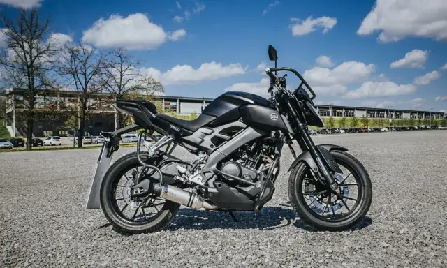 Czarny motocykl Yamaha, idealny na pierwsze prawo jazdy a1, stoi na żwirowym placu przed budynkiem.
