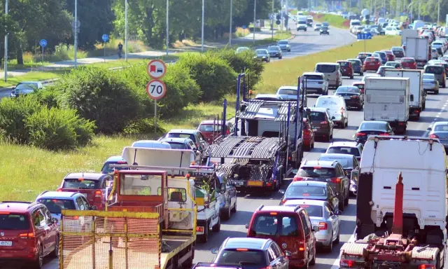 Korek na drodze, sznur samochodów i ciężarówek. Widać znak ograniczenia prędkości do 70. Może to być sytuacja wymagająca polisa car.