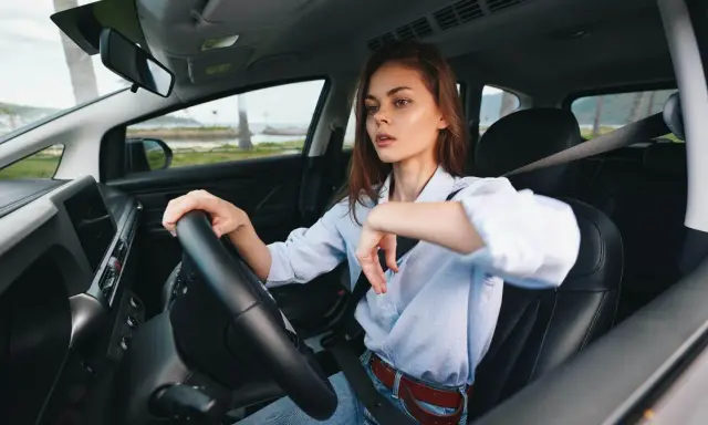 Kobieta za kierownicą zastanawia się, czy OC przedłuża się automatycznie. Widok na morze i palmy.