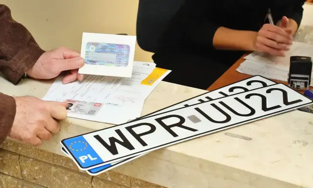 Nowe rejestracje samochodowe leżą na ladzie urzędu. Klient pokazuje dokumenty do rejestracji pojazdu.